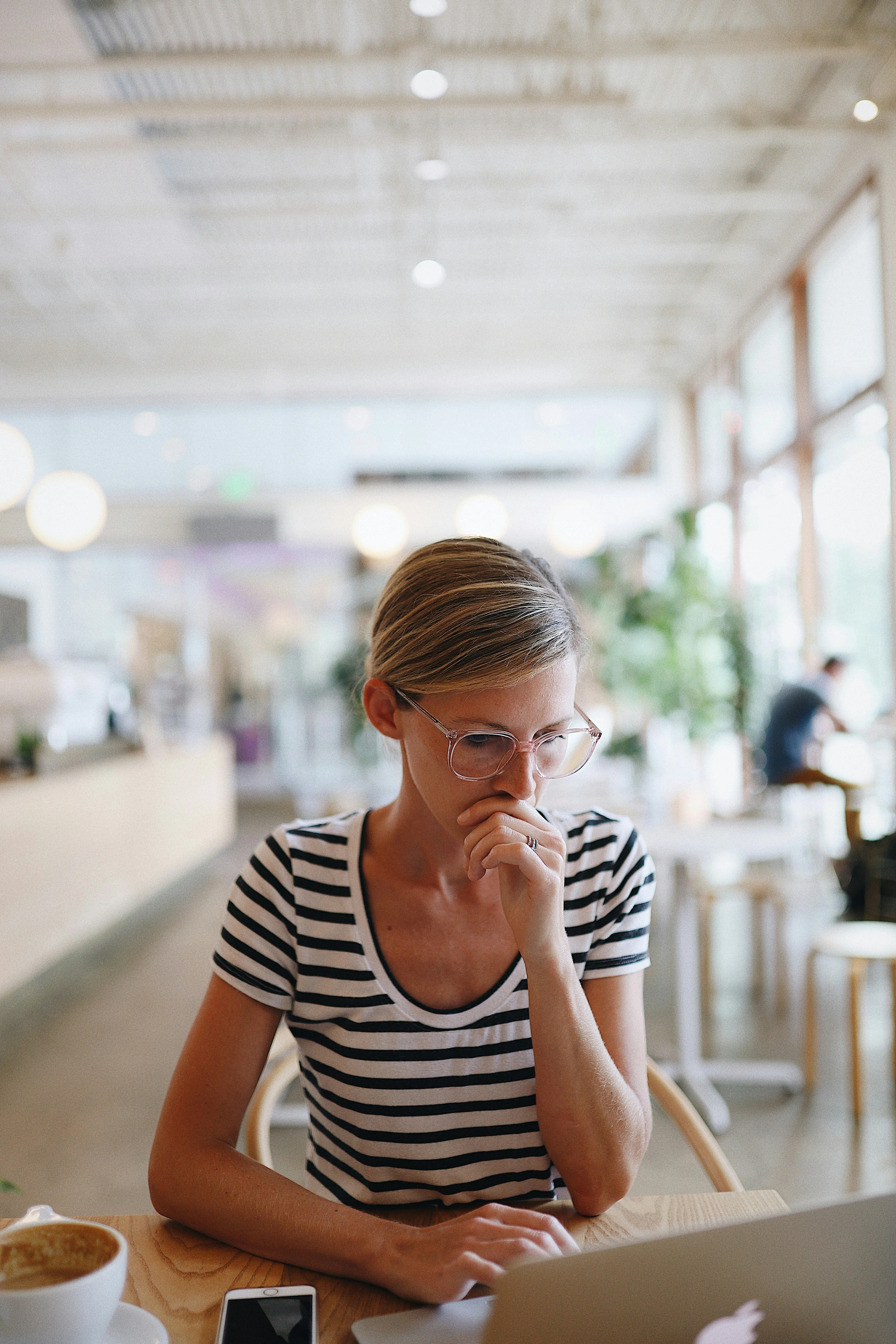 Female wearing glasses and looking at a laptop screen in an office considering the content in front of her. 