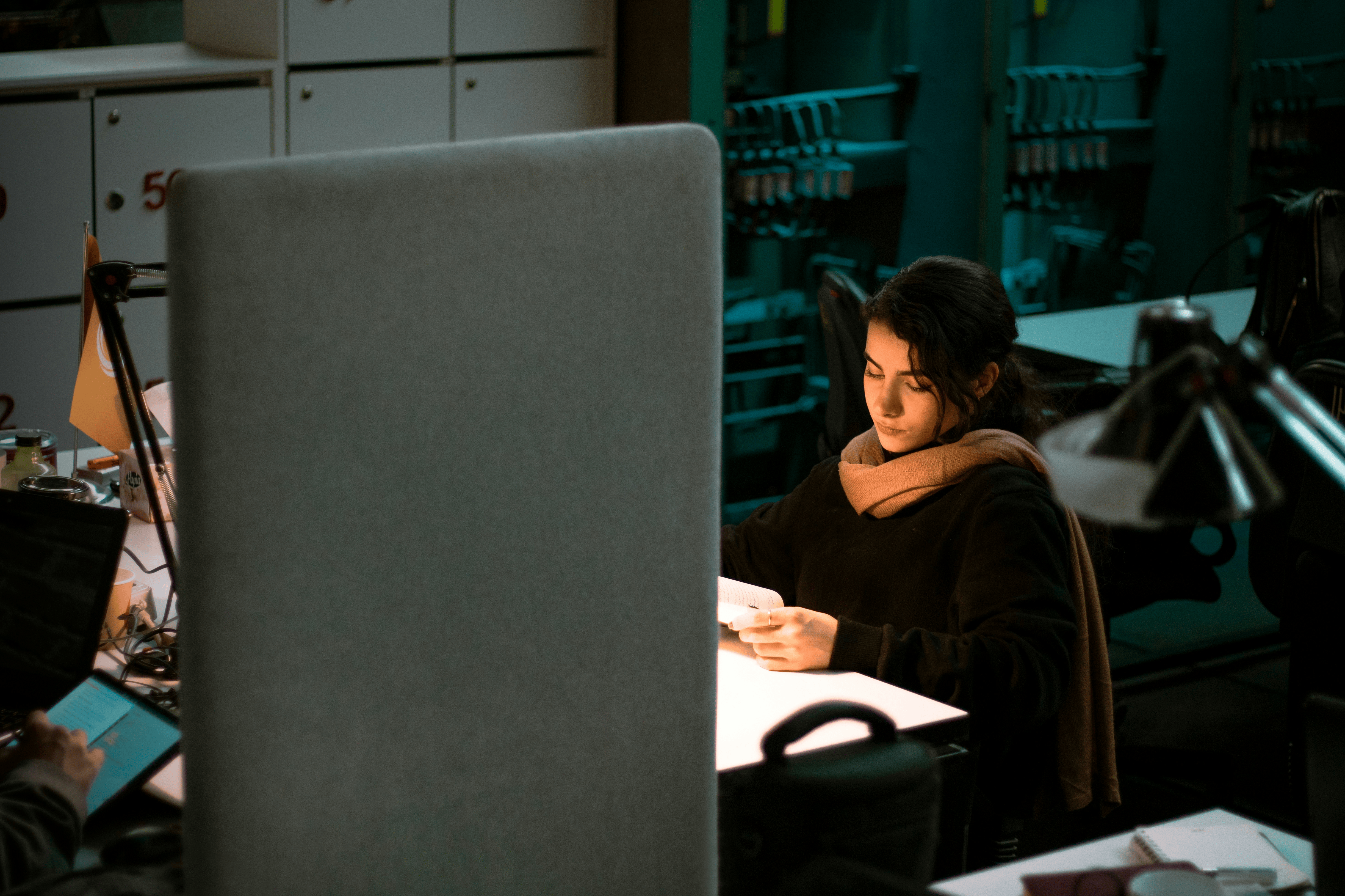 Image shows a female sitting at an office desk in a dimly lit environment, studying documents
