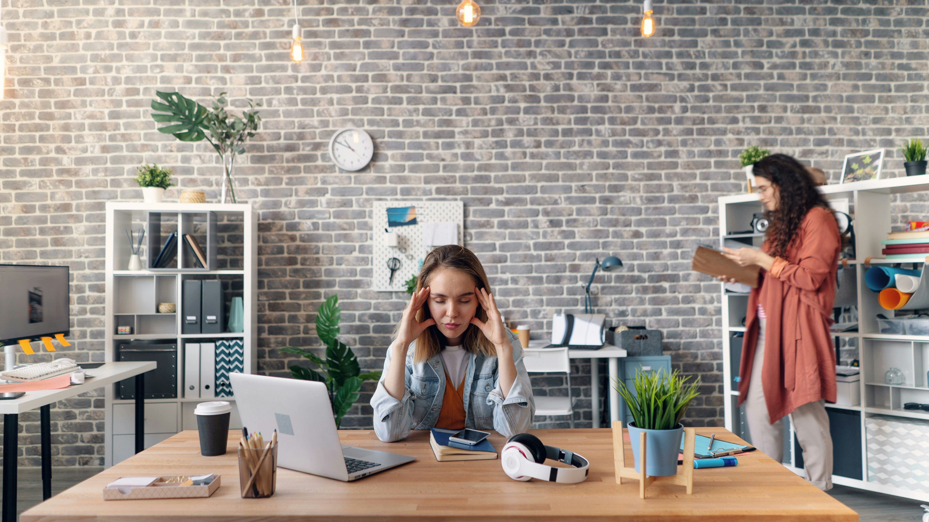 Image shows a female with her head ni her hadns, sitting at a desk in an office
