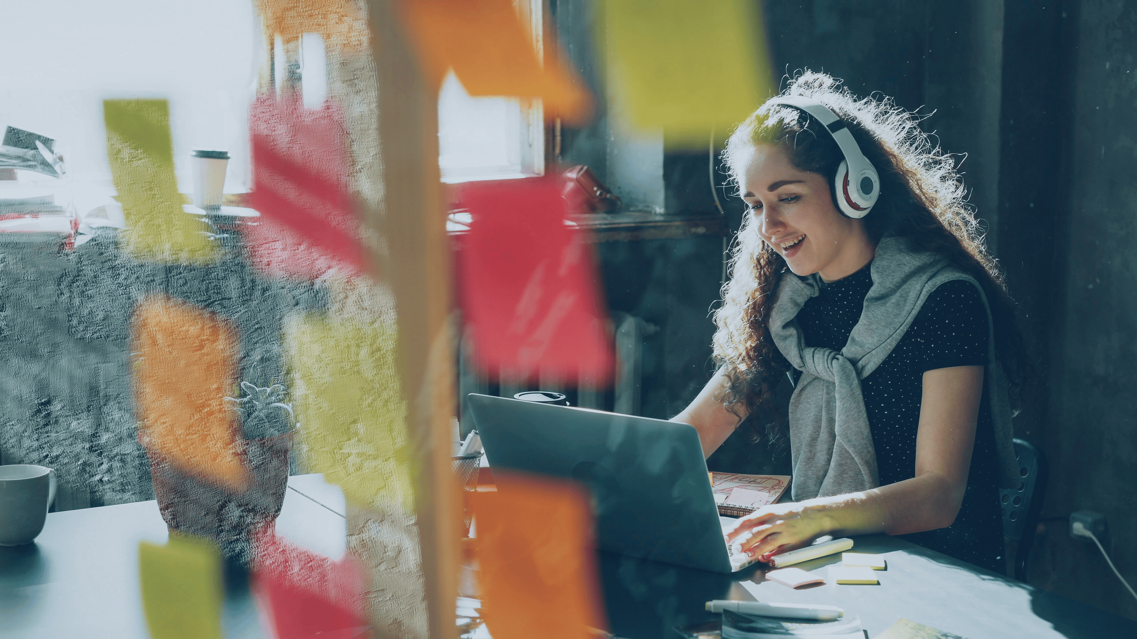 Image shows female in an office busy working uninterrupted with headphones on. She appears happy