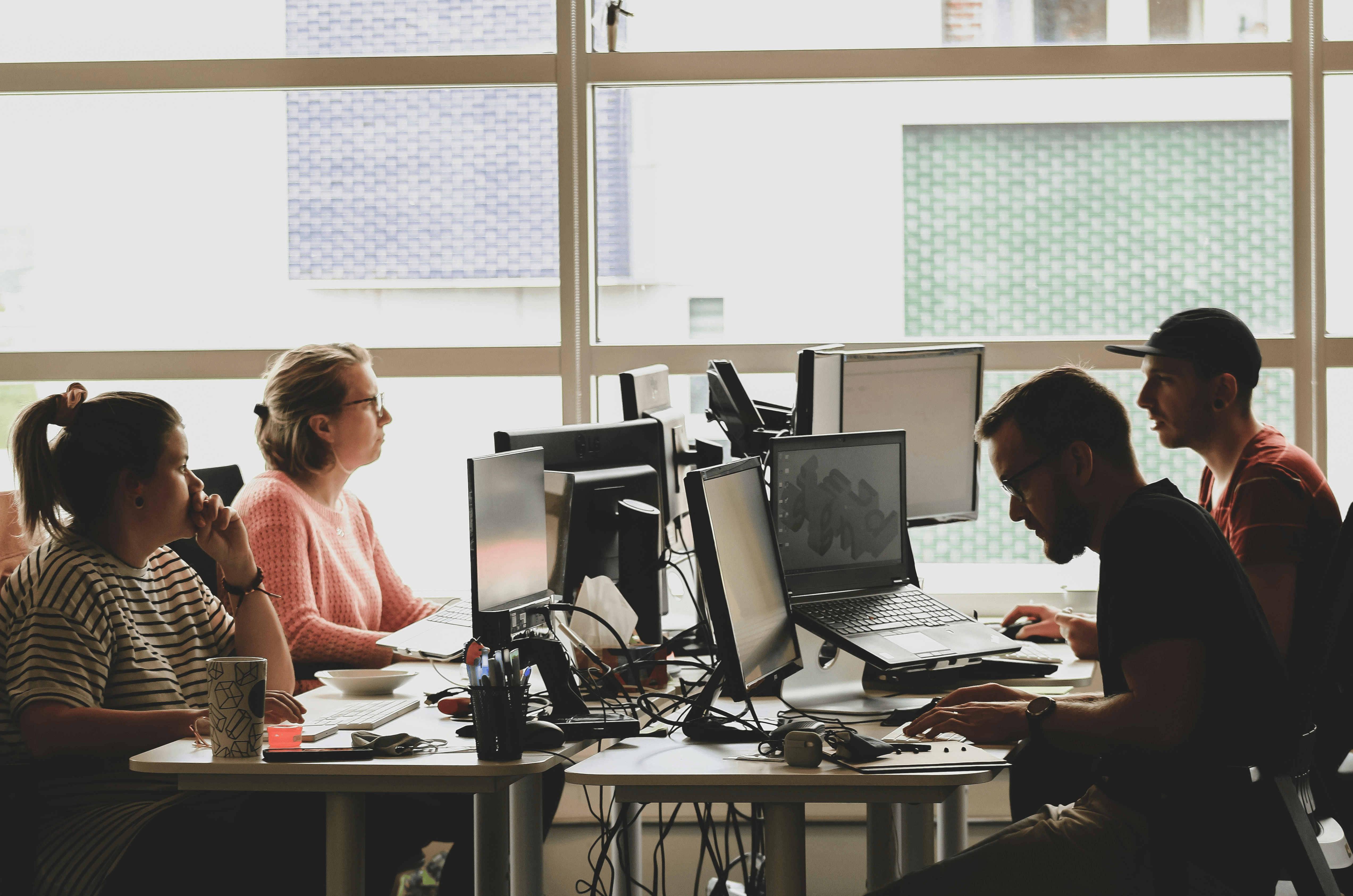 Image shows four people sat around a four desk formation in an office, working